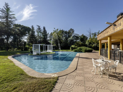 A nice pool with metal Balinese beds in the center and many trees in the garden